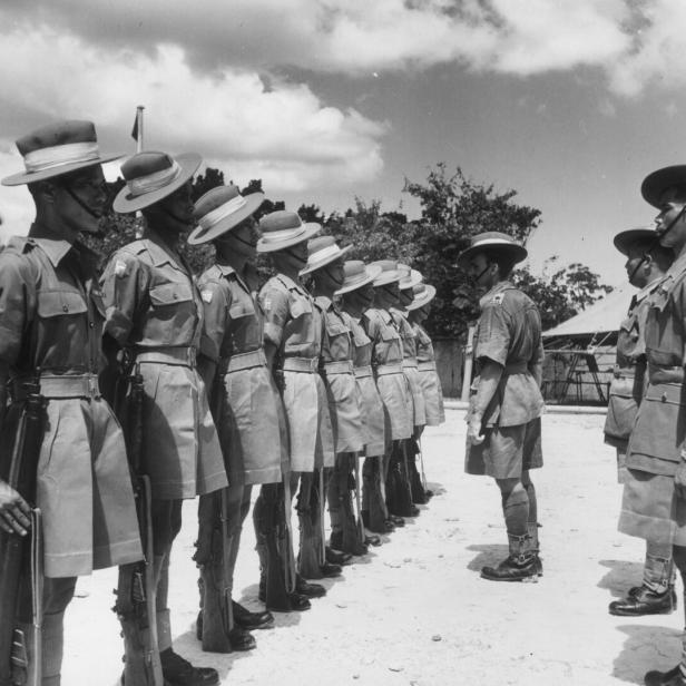 Soldaten in Uniform stehen in Reih und Glied und werden von einem Vorgesetzten auf dem Exerzierplatz inspiziert.