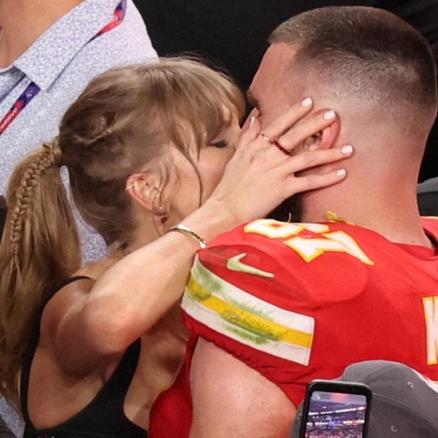 Taylor Swift küsst den Footballspieler Travis Kelce, der ein rotes Trikot der Kansas City Chiefs trägt.