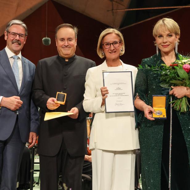 Vier Personen bei einer Preisverleihung, zwei mit Medaille und Urkunde, die Frau rechts hält einen Blumenstrauß.