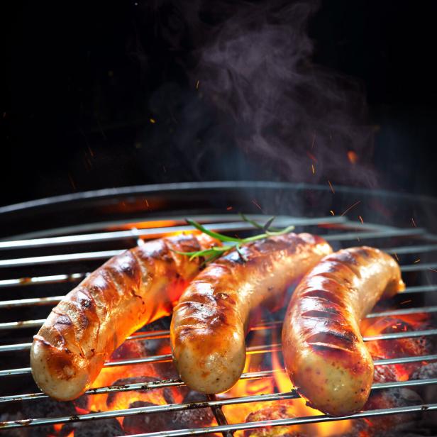 Grilled sausages on grill with smoke and flame