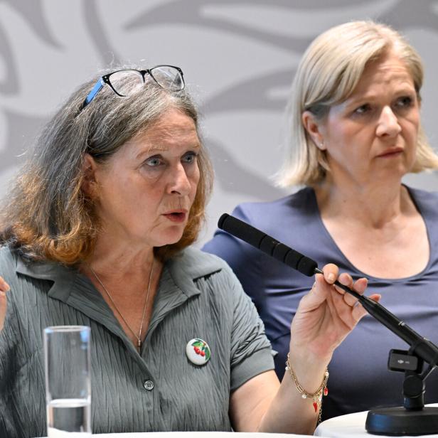 Zwei Frauen bei einer Pressekonferenz; die vordere spricht ins Mikrofon und hält einen Gegenstand hoch.