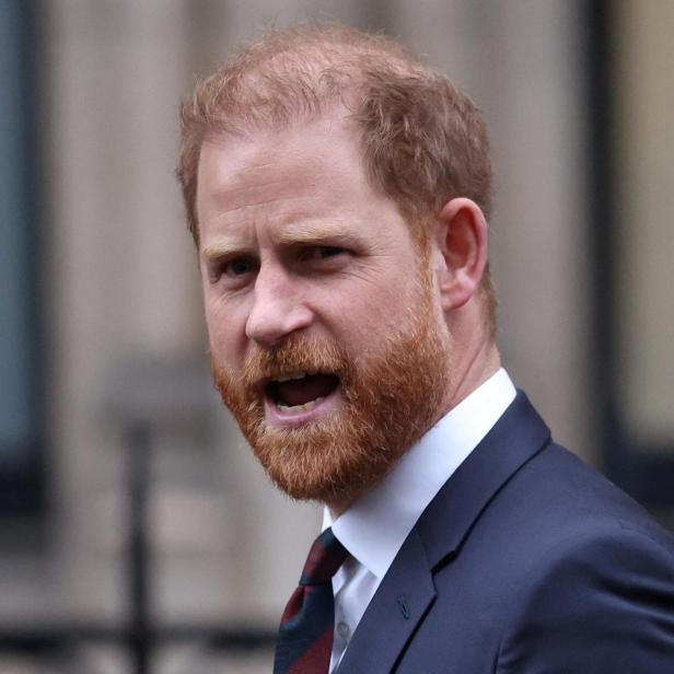 Prinz Harry trägt einen dunklen Anzug mit Krawatte und spricht mit offenem Mund vor einem unscharfen Hintergrund.