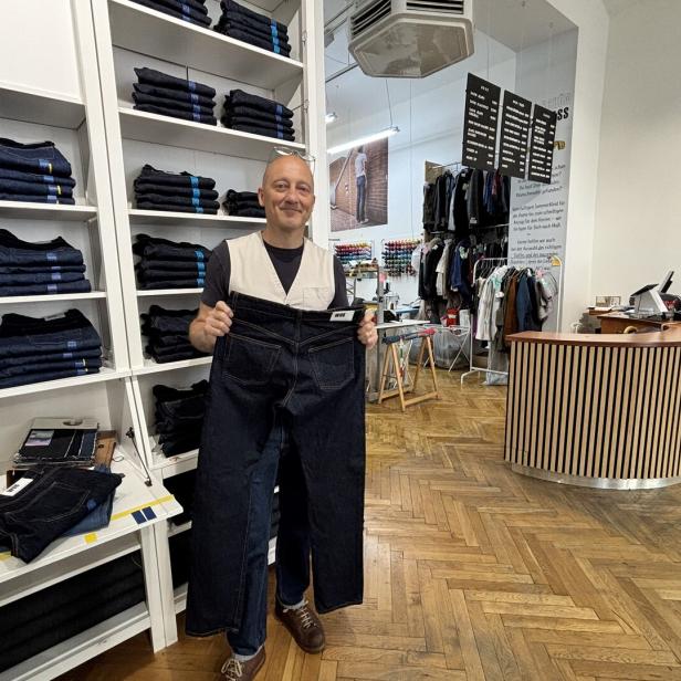 Mann in Jeansladen hält eine sehr große dunkle Jeans vor sich.