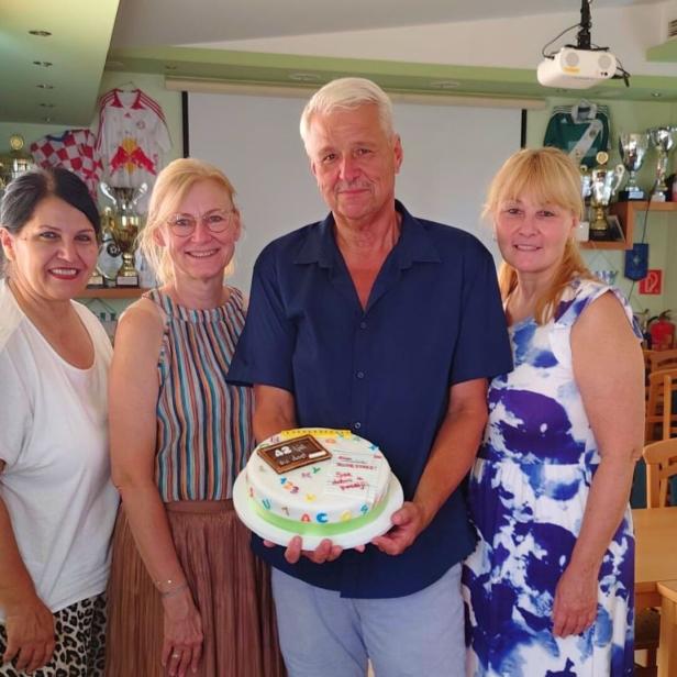 Drei Frauen und ein Mann stehen lächelnd zusammen, während der Mann eine Torte mit der Aufschrift „42“ hält.