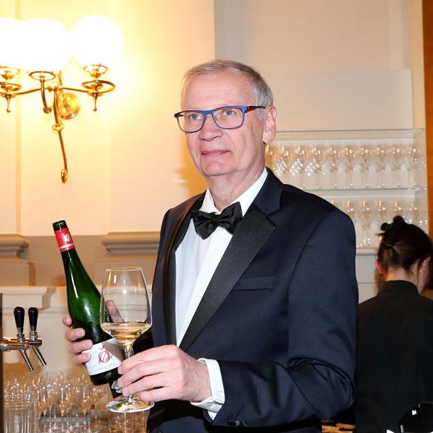 Günther Jauch im Smoking hält bei einem Empfang eine Weinflasche und ein gefülltes Glas in der Hand.
