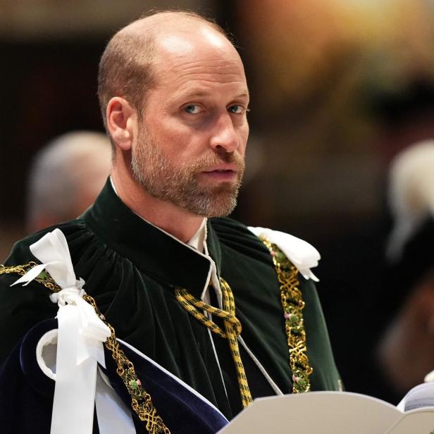 Prinz William trägt in zeremonieller Kleidung mit grünem Umhang und goldener Kette ein Programmheft in den Händen.