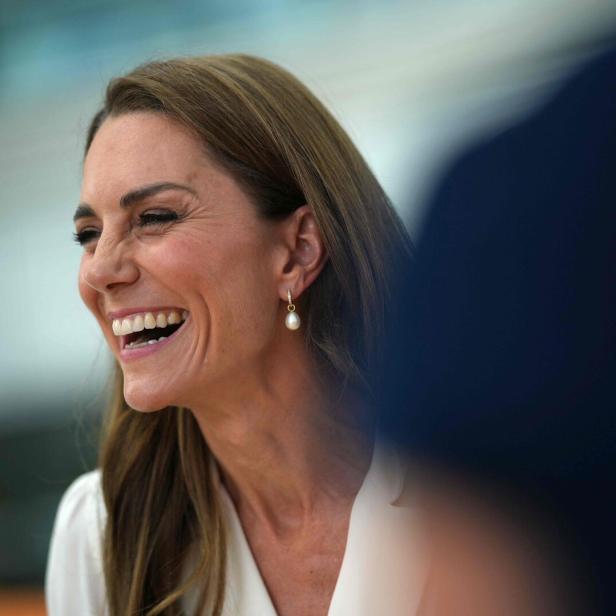 Prinzessin Kate lacht herzlich in einem hellen Oberteil mit Perlenohrringen.