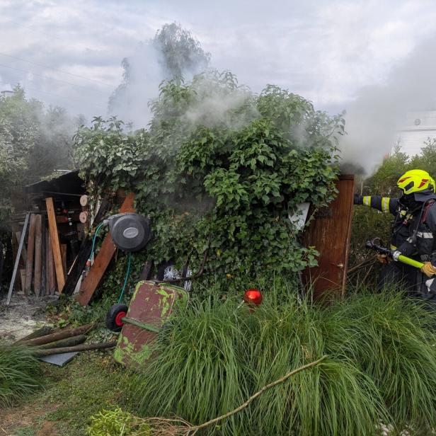 Feuerwehrmann löscht Rauch an einem stark bewachsenen Schuppen im Garten.