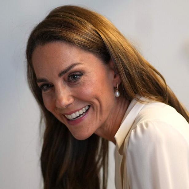 Prinzessin Kate lächelt freundlich in die Kamera und trägt eine weiße Bluse sowie Perlenohrringe.