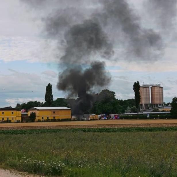 Dichter schwarzer Rauch steigt hinter Gebäuden auf, offenbar ein Brand auf einem Gelände im Grünen.