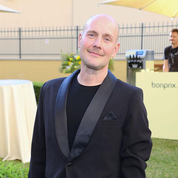 Oliver Petszokat alias Oli.P steht in schwarzem Anzug bei einem Event im Freien.