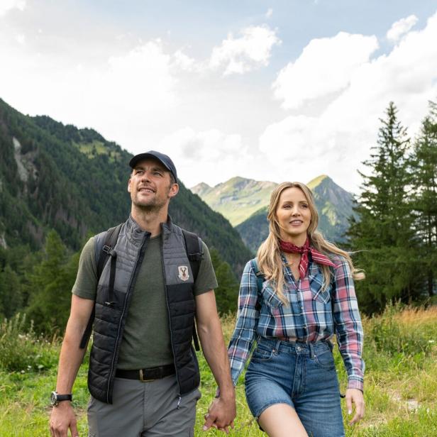 Ein Paar wandert Hand in Hand durch eine alpine Berglandschaft.