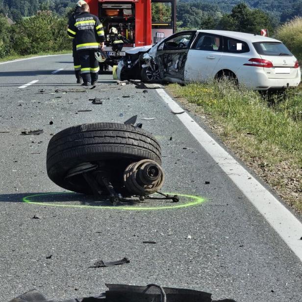 Schwerer Verkehrsunfall mit zerstörtem Auto, Feuerwehr, Trümmern und abgerissenem Rad auf der Straße.