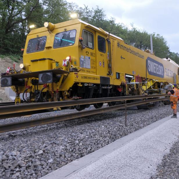 Gelbe Gleisbaumaschine mit Arbeitern auf einer Bahnstrecke im Wald.
