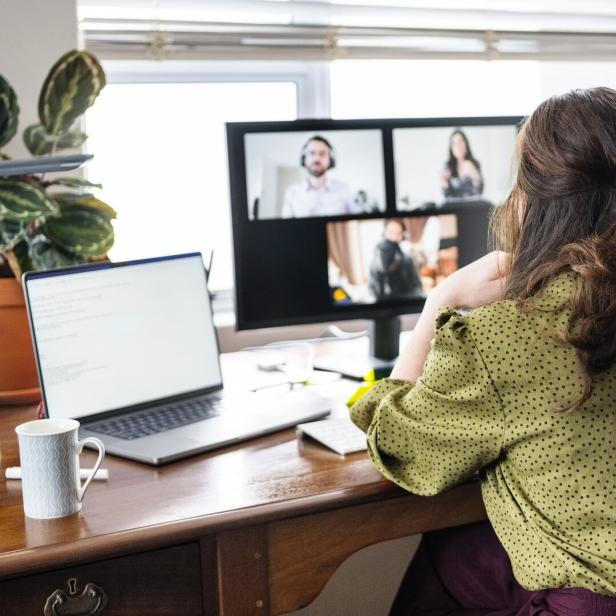Frau im Homeoffice vor Laptop und Monitor bei Videokonferenz.
