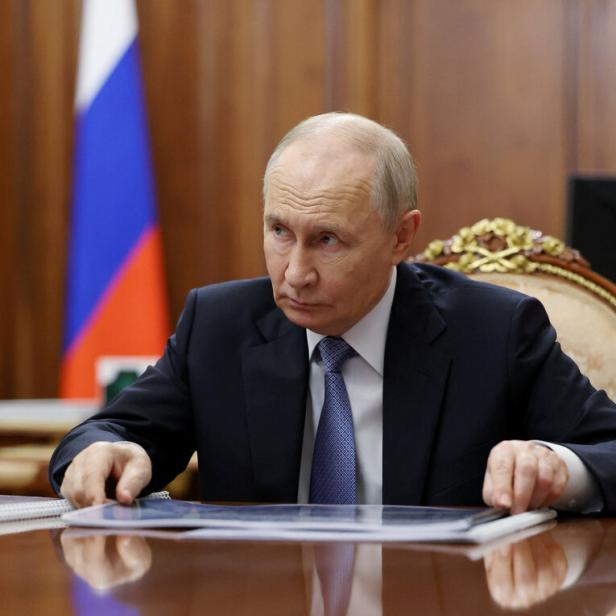 Wladimir Putin sitzt an einem Konferenztisch vor einer russischen Flagge und blickt auf Dokumente.