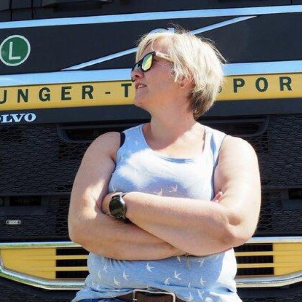 Eine Frau mit Sonnenbrille lehnt vor einem gelben Volvo-Lkw mit verschränkten Armen.