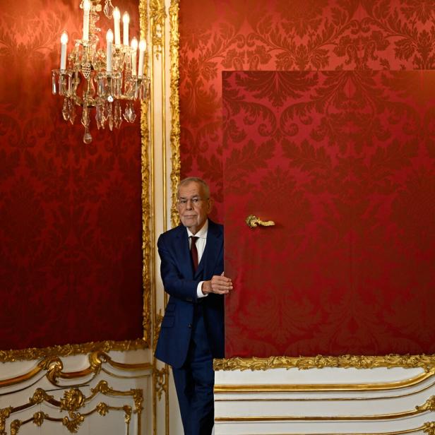 Der österreichische Bundespräsident Alexander Van der Bellen steht in einem prunkvollen Raum mit roter Tapete hinter einer halb geöffneten Tür.