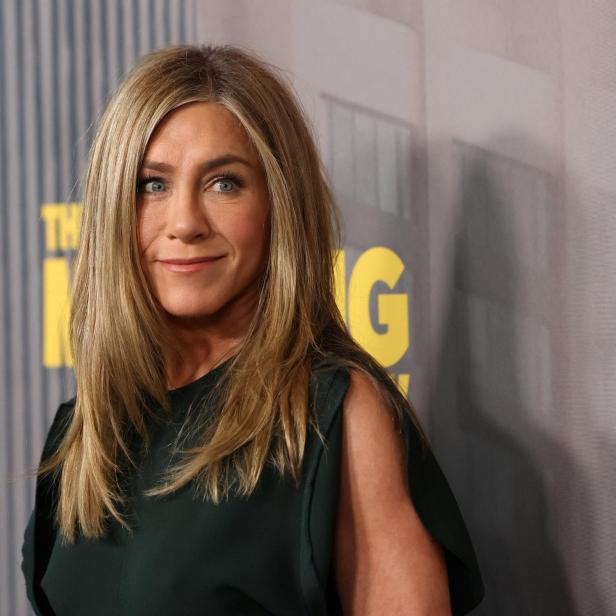 Jennifer Aniston lächelt vor einem Hintergrund mit dem Schriftzug „The Morning Show“.
