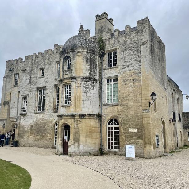 Ein historisches Schloss aus hellem Stein mit einem markanten Rundturm unter einem bewölkten Himmel.