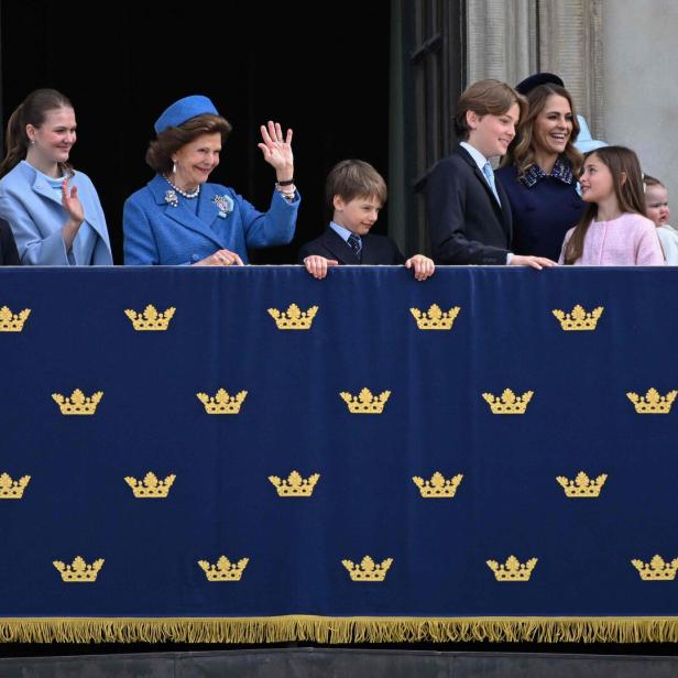 Die schwedische Königsfamilie mit Königin Silvia winkt von einem mit Kronen verzierten Balkon des Stockholmer Schlosses der Menge zu.