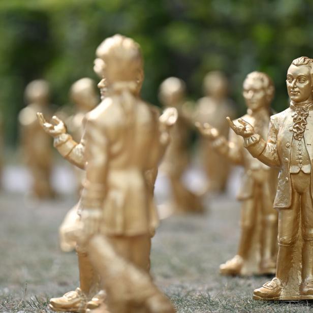 Zahlreiche goldene Mozart-Statuen stehen in einer Parkanlage auf einer Wiese.