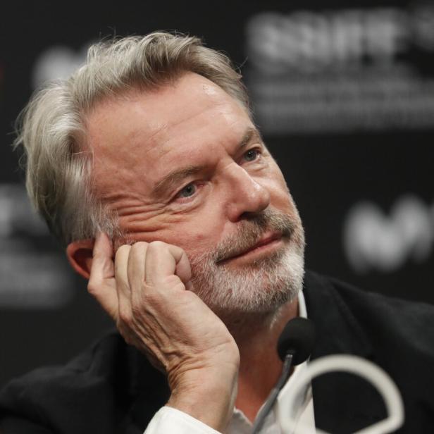 Der Schauspieler Sam Neill stützt nachdenklich seinen Kopf auf die Hand.