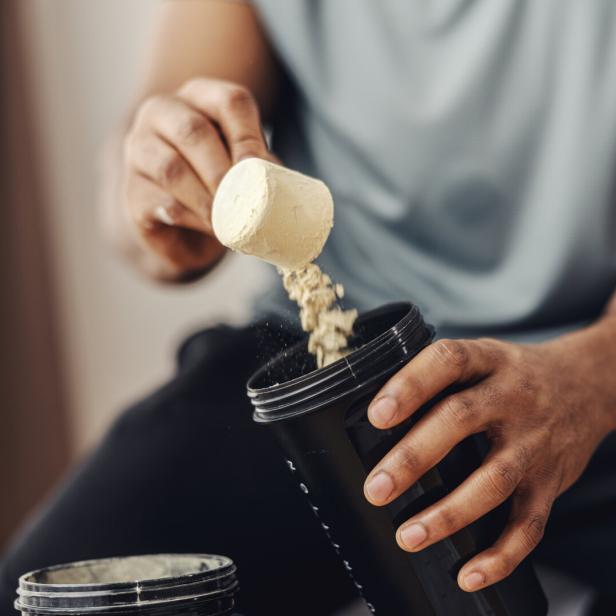Person adding protein powder to shaker for fitness