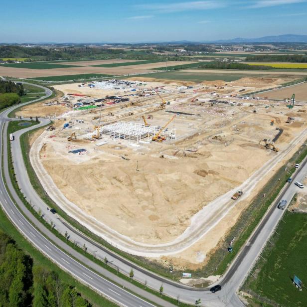 Luftaufnahme einer großen Baustelle inmitten von Feldern mit Kränen, Baggern und neuem Hallenbau.