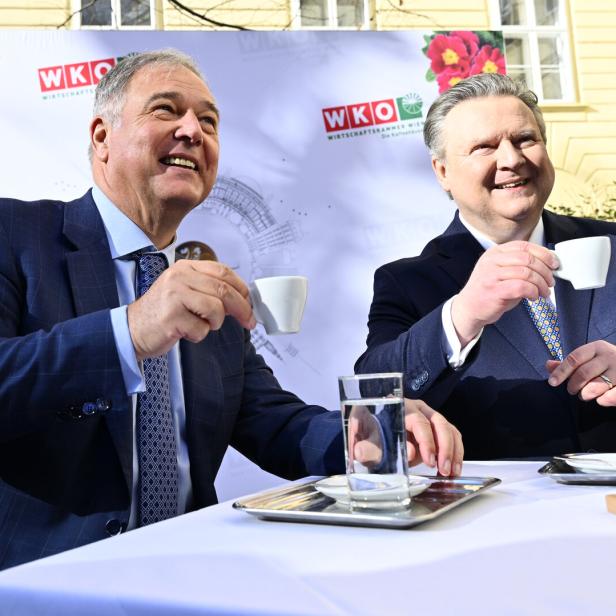 Walter Ruck und Michael Ludwig im Anzug trinken im Freien Espresso an einem Tisch vor einem WKO-Hintergrund.