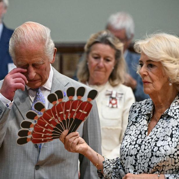 König Charles III. wischt sich eine Träne aus dem Auge, während Königin Camilla einen Fächer mit Motiven britischer Gardesoldaten hält.
