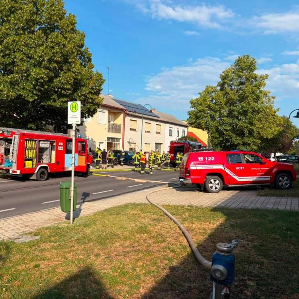 Feuerwehrkräfte und Einsatzfahrzeuge sichern eine Straße mit ausgelegtem Schlauch vor Wohnhäusern.