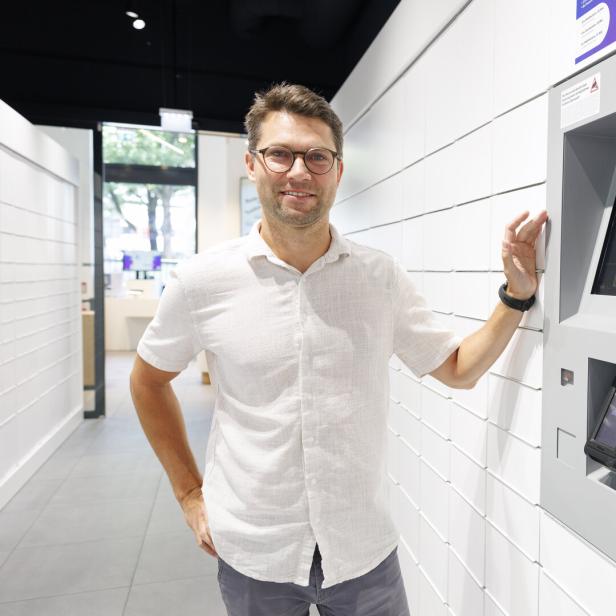 Mann in weißem Hemd neben einem interaktiven Automaten in modernem Raum.
