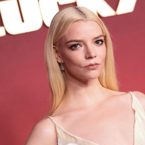 Anya Taylor-Joy mit blondem Haar vor einem roten Hintergrund.