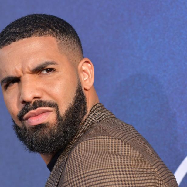 Der Rapper Drake blickt mit kurzem Haar und gepflegtem Bart vor einem blauen Hintergrund zur Seite.