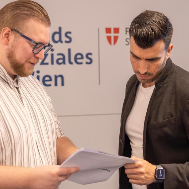 Zwei Männer besprechen Unterlagen vor dem Fonds-Soziales-Wien-Logo.