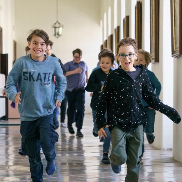 Kinder laufen fröhlich durch einen Klostergang.