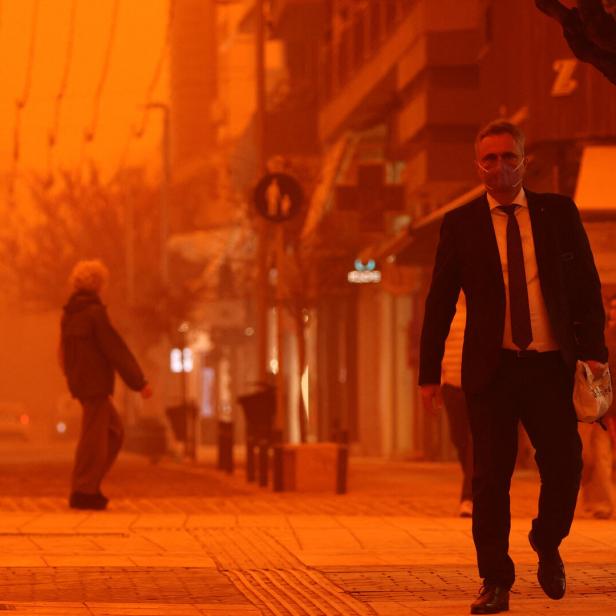 Ein Mann im Anzug mit Schutzmaske geht auf einer Straße in Heraklion auf Kreta. Die Luft ist durch Sahara-Staub orange gefärbt. 