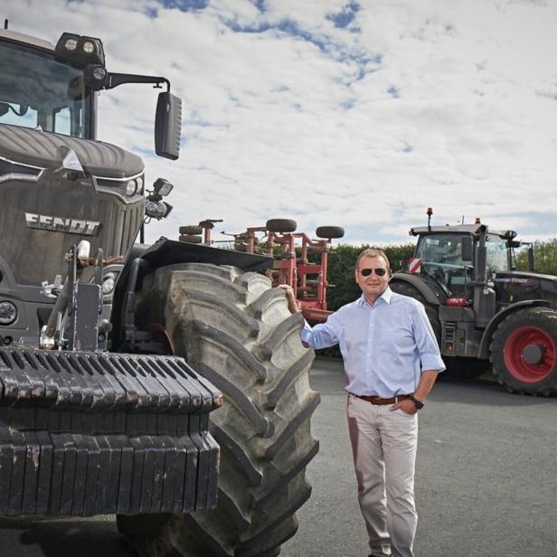 Mann in hellblauem Hemd steht neben großem Fendt-Traktor auf einem Hof.