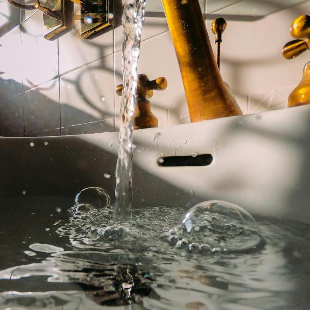 Wasser strömt aus einem goldfarbenen Hahn in ein Becken und steht für die Abwasserreinigung und den Wasserkreislauf.