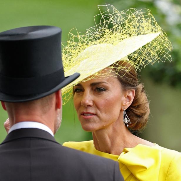 Prinzessin Kate trägt ein gelbes Kleid und einen auffälligen Hut, während sie mit William im Zylinder spricht.