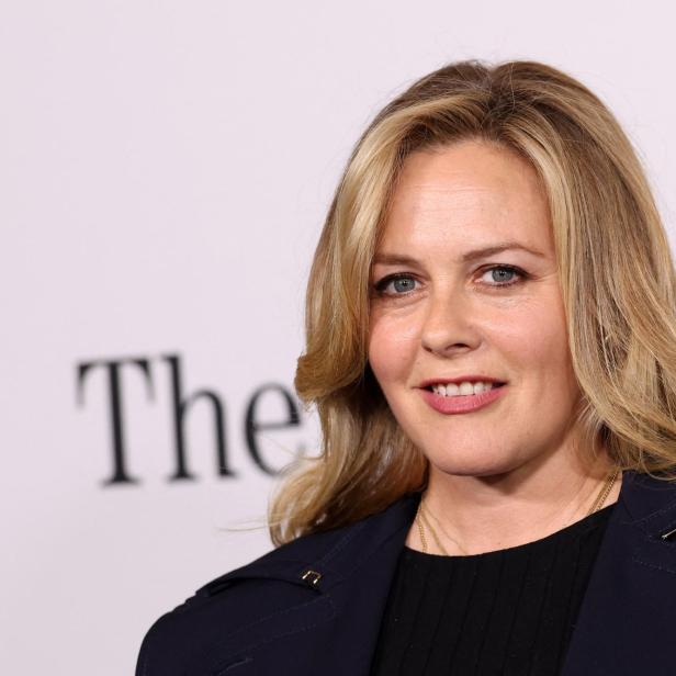Alicia Silverstone lächelt vor einem hellen Hintergrund mit dem Schriftzug „The“ in die Kamera.