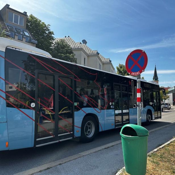 Stadtbus hält an Haltestelle neben Parkverbotsschild und grüner Mülltonne.