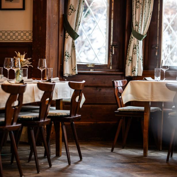 Gemütliches Restaurant mit gedeckten Tischen, Holzstühlen und großen Fenstern.
