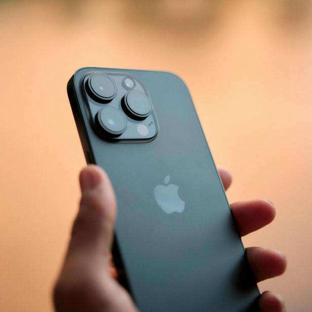 Hand hält ein schwarzes Smartphone mit drei Kameralinsen und einem Apfel-Logo auf der Rückseite.