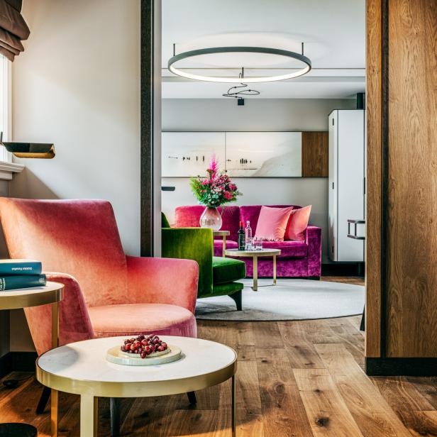 Elegantes Wohnzimmer mit rosafarbenem Sessel, grünen und pinken Sofas, Blumen und modernen Tischen.