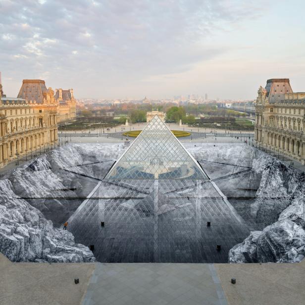 Die Glaspyramide des Louvre in Paris ist von einer großflächigen, schwarz-weißen Bodeninstallation umgeben, die eine felsige Landschaft darstellt.