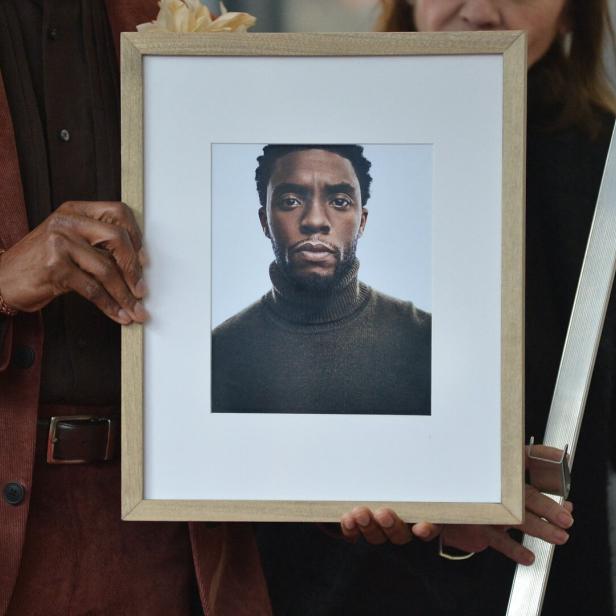 Personen halten einen gerahmten Porträtabzug des verstorbenen Schauspielers Chadwick Boseman in den Händen.