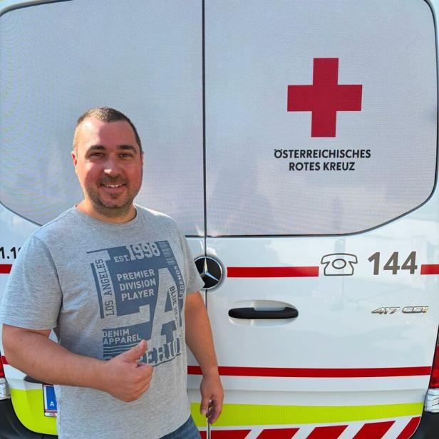 Mann lächelt vor einem Rettungswagen des Österreichischen Roten Kreuzes und zeigt den Daumen hoch.