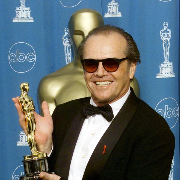 Jack Nicholson lächelt mit Sonnenbrille und Smoking vor einem blauen ABC-Hintergrund und hält eine goldene Oscar-Trophäe in der Hand.